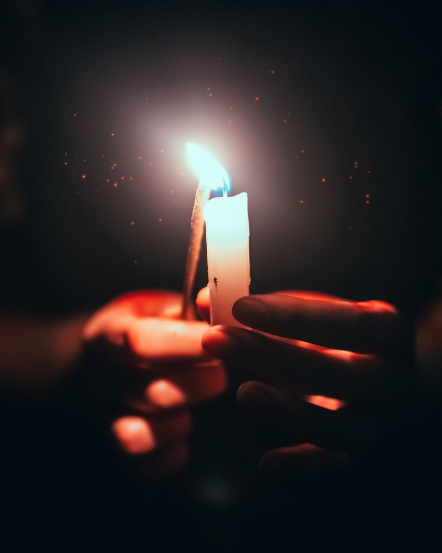 Mãos segurando uma vela acesa, simbolizando memória, conforto e respeito